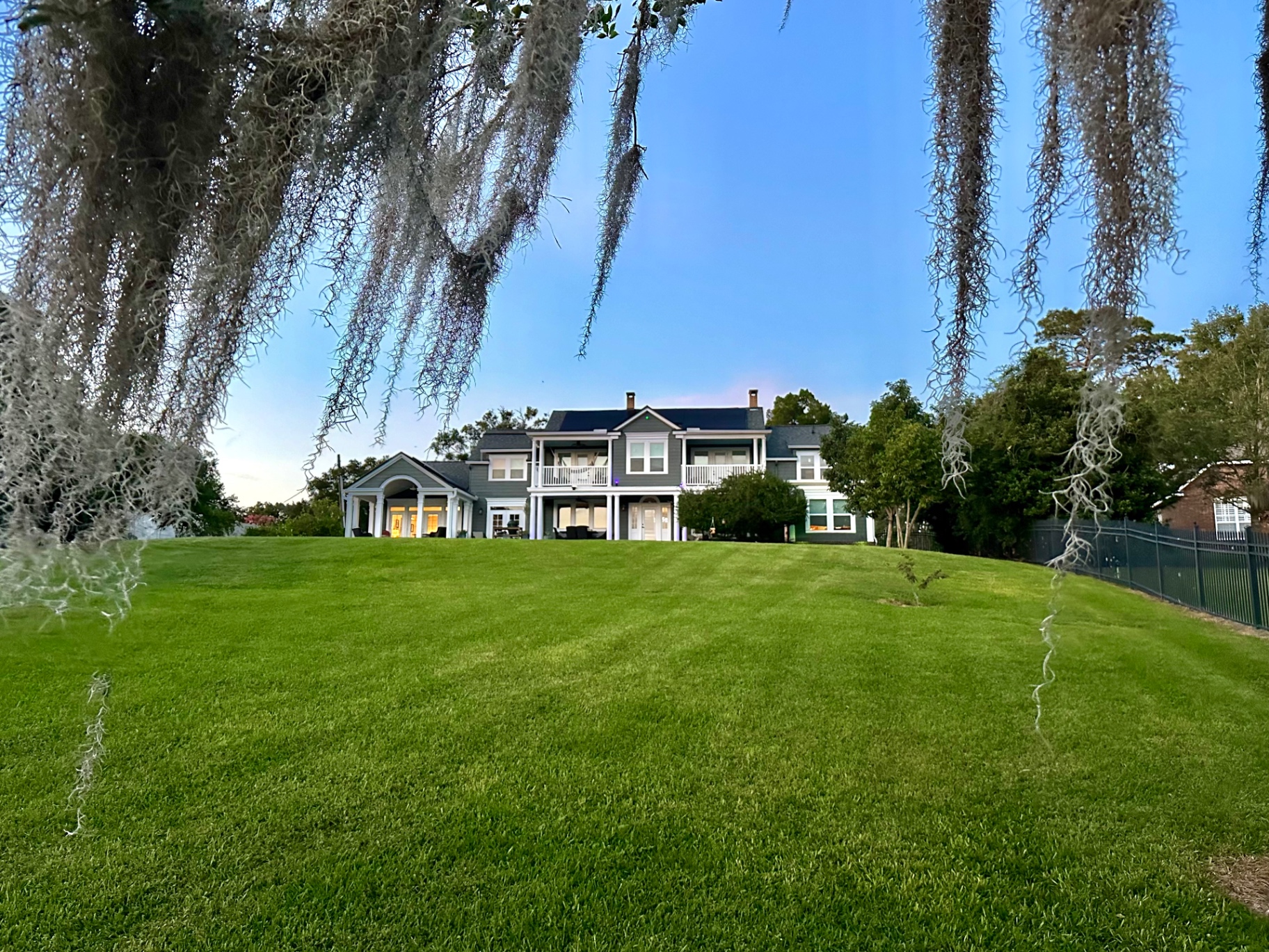 The Berry House estate at dusk, seen across a wide lawn and framed by oaks draped in Spanish moss